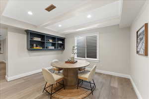 Dining area with light wood-type flooring, baseboards, visible vents, and beamed ceiling
