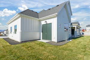 Rear view of house featuring roof with shingles, a yard, and board and batten siding
