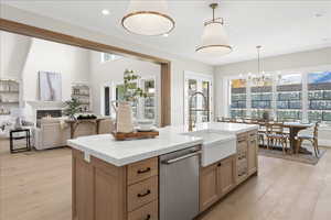 Kitchen with light wood finished floors, stainless steel dishwasher, light stone counters, and a sink