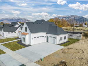 View of front facade featuring a shingled roof, a front lawn, concrete driveway, an attached garage, and a mountain view