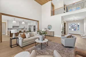 Living room with light wood finished floors, baseboards, a towering ceiling, an inviting chandelier, and recessed lighting