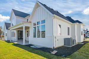 Rear view of property featuring a ceiling fan, central AC unit, board and batten siding, a patio, and a lawn