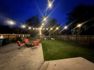 Yard at night with cafe lights, a patio and a fenced backyard