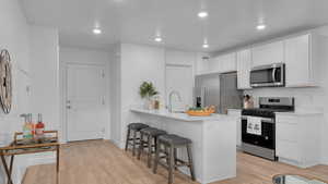 Kitchen featuring a kitchen bar, stainless steel appliances, light wood-style flooring, and a sink