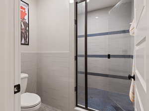 Full bath with tile walls, wainscoting, a shower stall, and toilet