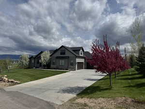 View of front of house featuring stone siding, driveway, a front yard, and a garage