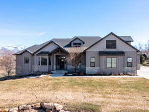 Modern inspired farmhouse with a standing seam roof, a front lawn, stone siding, board and batten siding, and roof with shingles
