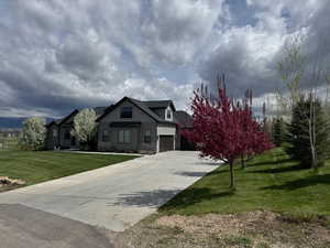 View of front facade with stone siding, driveway, and a front lawn