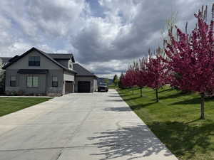 View of front of home featuring a front lawn, board and batten siding, driveway, stone siding, and an attached garage