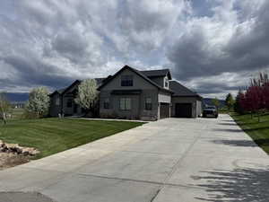 View of front facade with board and batten siding, concrete driveway, a front yard, stone siding, and an attached garage