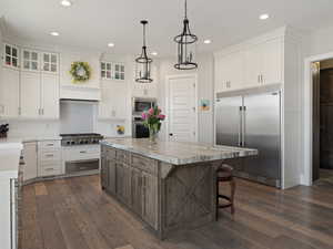 Kitchen with built in appliances, light countertops, white cabinets, and a center island