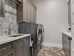 Washroom with a sink, cabinet space, baseboards, washer and dryer, and brick floor