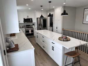 Kitchen featuring wood finished floors, stainless steel appliances, a kitchen island, and white cabinetry