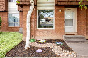 Entrance to property with central AC, mansard roof, and brick siding
