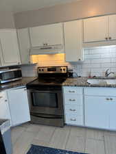 Kitchen with appliances with stainless steel finishes, white cabinets, under cabinet range hood, and decorative backsplash