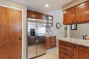 Kitchen featuring light floors, light stone counters, brown cabinets, and stainless steel fridge