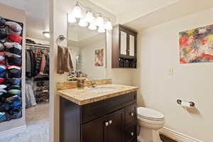 Bathroom featuring toilet, a spacious closet, vanity, and baseboards