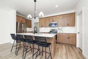 Kitchen featuring light wood-style flooring, a sink, appliances with stainless steel finishes, a breakfast bar, and a kitchen island with sink