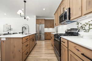Kitchen featuring a sink, stainless steel appliances, light wood-type flooring, a center island with sink, and light countertops