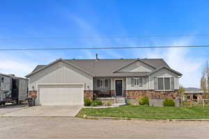 Ranch-style house with a front yard, stone siding, roof with shingles, concrete driveway, and an attached garage