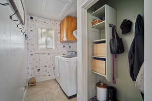 Laundry room with cabinet space, light tile patterned flooring, separate washer and dryer, baseboards, and wallpapered walls