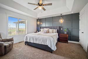 Bedroom featuring carpet flooring, a raised ceiling, visible vents, a decorative wall, and baseboards