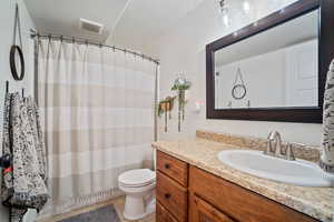 Bathroom with tile patterned floors, toilet, curtained shower, vanity, and visible vents
