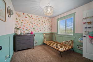 Carpeted bedroom featuring an inviting chandelier and a wainscoted wall