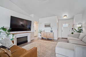 Living area featuring a fireplace, wood finished floors, baseboards, arched walkways, and lofted ceiling