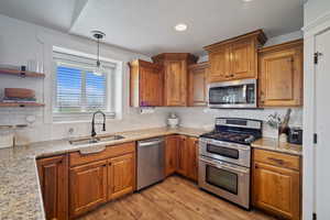 Kitchen featuring tasteful backsplash, a sink, stainless steel appliances, light wood-type flooring, and brown cabinetry