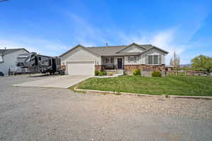 Single story home with a front yard, stone siding, concrete driveway, an attached garage, and fence