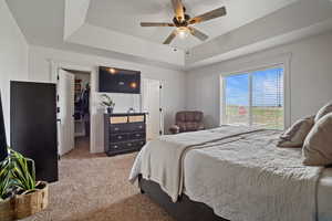 Carpeted bedroom with a ceiling fan, a walk in closet, a closet, and a raised ceiling