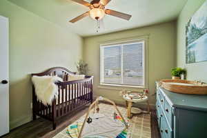 Bedroom with baseboards, wood finished floors, ceiling fan, and a nursery area