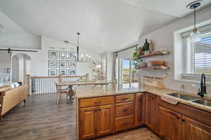 Kitchen with brown cabinets, a sink, a peninsula, vaulted ceiling, and arched walkways