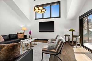 Living room featuring wood finished floors, a wealth of natural light, a towering ceiling, and a notable chandelier