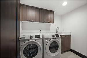 Clothes washing area featuring cabinet space, baseboards, a sink, and separate washer and dryer