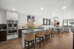Kitchen featuring stainless steel appliances, modern cabinets, a sink, wall chimney exhaust hood, and a kitchen bar