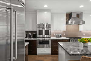 Kitchen with wall chimney exhaust hood, modern cabinets, dark brown cabinetry, and appliances with stainless steel finishes