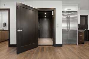 Interior space with baseboards, dark wood-style flooring, elevator, and stainless steel built in fridge