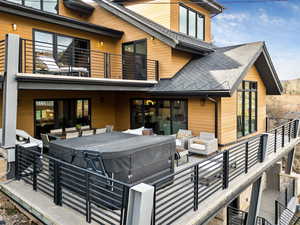 Rear view of house featuring roof with shingles, a balcony, an outdoor hangout area, and a hot tub