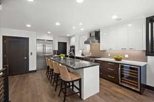 Kitchen featuring wall chimney exhaust hood, stainless steel appliances, a sink, a kitchen bar, and beverage cooler