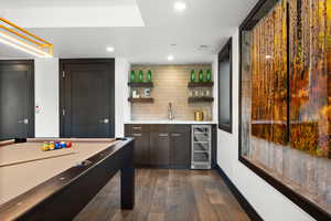 Bar featuring dark wood finished floors, beverage cooler, backsplash, a sink, and indoor wet bar