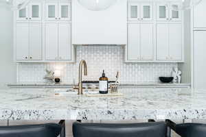 Kitchen with a kitchen bar, white cabinetry, light stone countertops, and tasteful backsplash