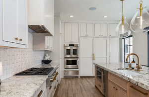 Kitchen with light wood-style flooring, appliances with stainless steel finishes, a warming drawer, a sink, and premium range hood