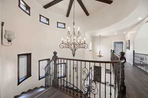 Stairway with beamed ceiling, a high ceiling, a notable chandelier, and wood finished floors