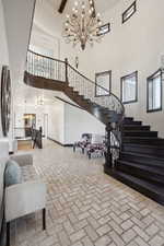 Interior space with an inviting chandelier, stairs, brick floor, visible vents, and a high ceiling