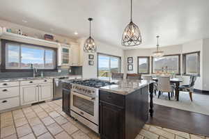Kitchen with light stone counters, decorative backsplash, glass insert cabinets, appliances with stainless steel finishes, and hanging light fixtures