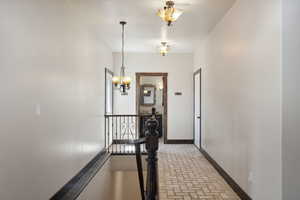 Corridor featuring an upstairs landing, an inviting chandelier, brick floor, and baseboards