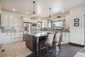 Kitchen with decorative backsplash, visible vents, light stone counters, a kitchen island, and appliances with stainless steel finishes