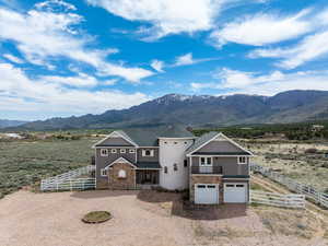 View of front of house with fence, dirt driveway, stone siding, a mountain view, and an attached garage